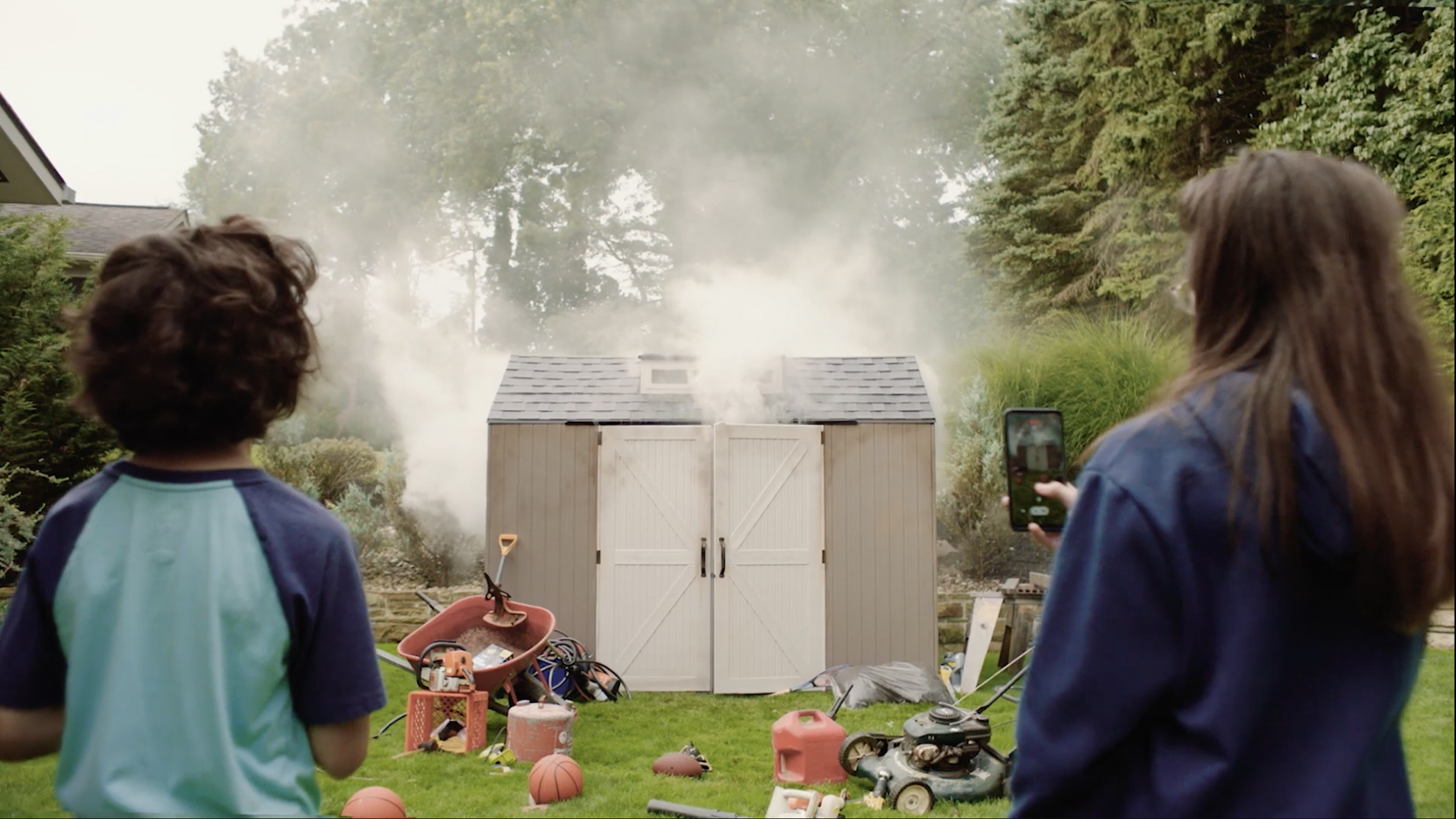 Two kids looking at a shed with smoke coming out of it.